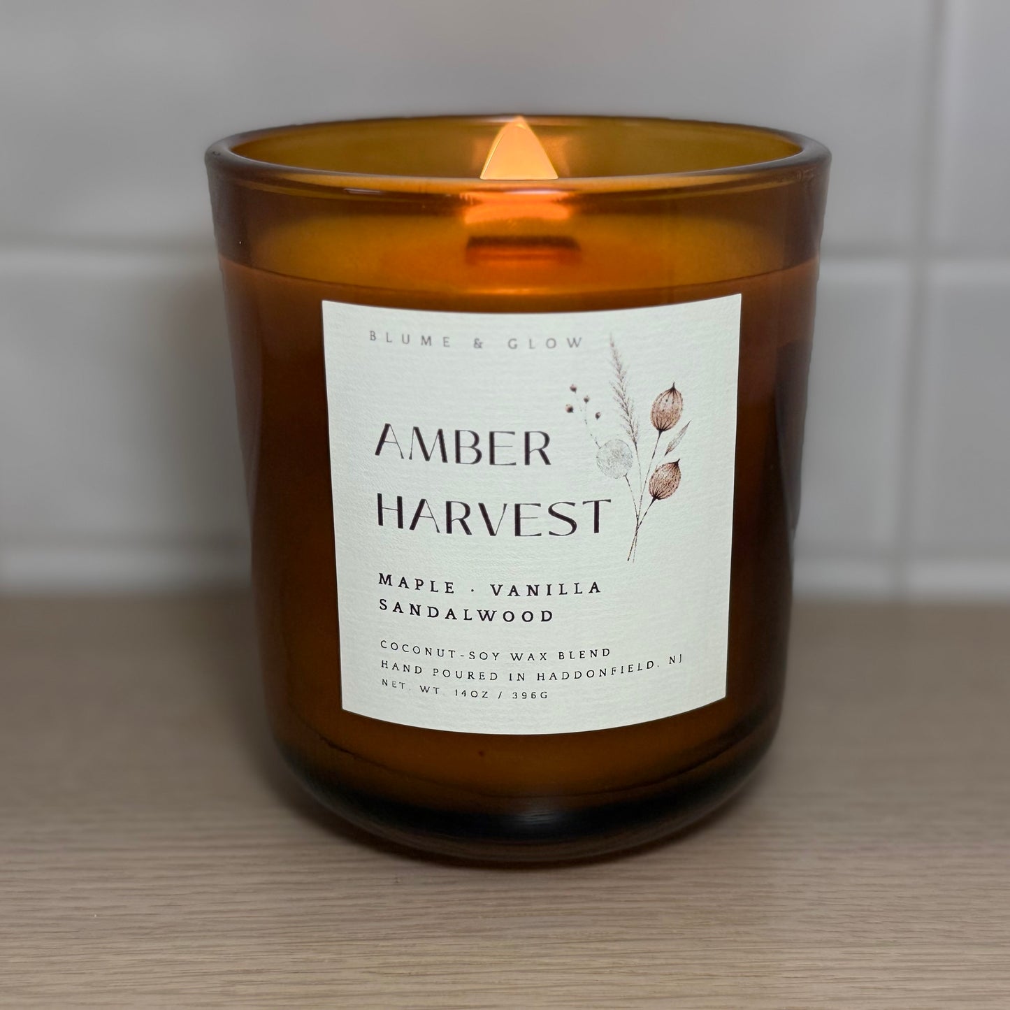 Amber Harvest candle burning with a glowing wooden wick in an amber glass vessel.