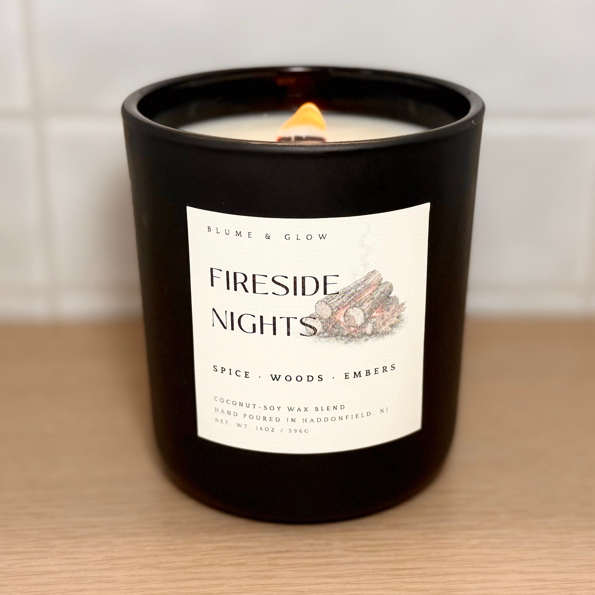 Fireside Nights candle burning with a glowing wooden wick in a matte black glass vessel.