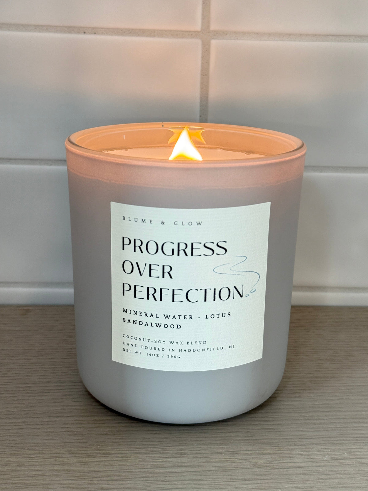 Blume & Glow Progress Over Perfection candle lit in a gray jar with wooden wick.